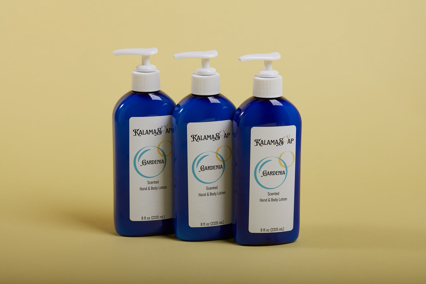 A photo of 3, 8-fluid ounce blue lotion bottles with white pumps on a yellow background labelend KalamaSoap Gardenia Scented Hand & Body Lotion